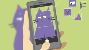 An illustration showing a hand holding a smartphone with its camera app open, capturing an image of a cartoon purple cat. The camera screen displays the cat framed with a square outline, and several facial features—such as the eyes, ears, and nose—are highlighted with smaller boxes and connected by thin lines, illustrating an AI recognition process. The cat is slightly blurred in the background outside the phone screen, emphasising the focus on the camera's view.